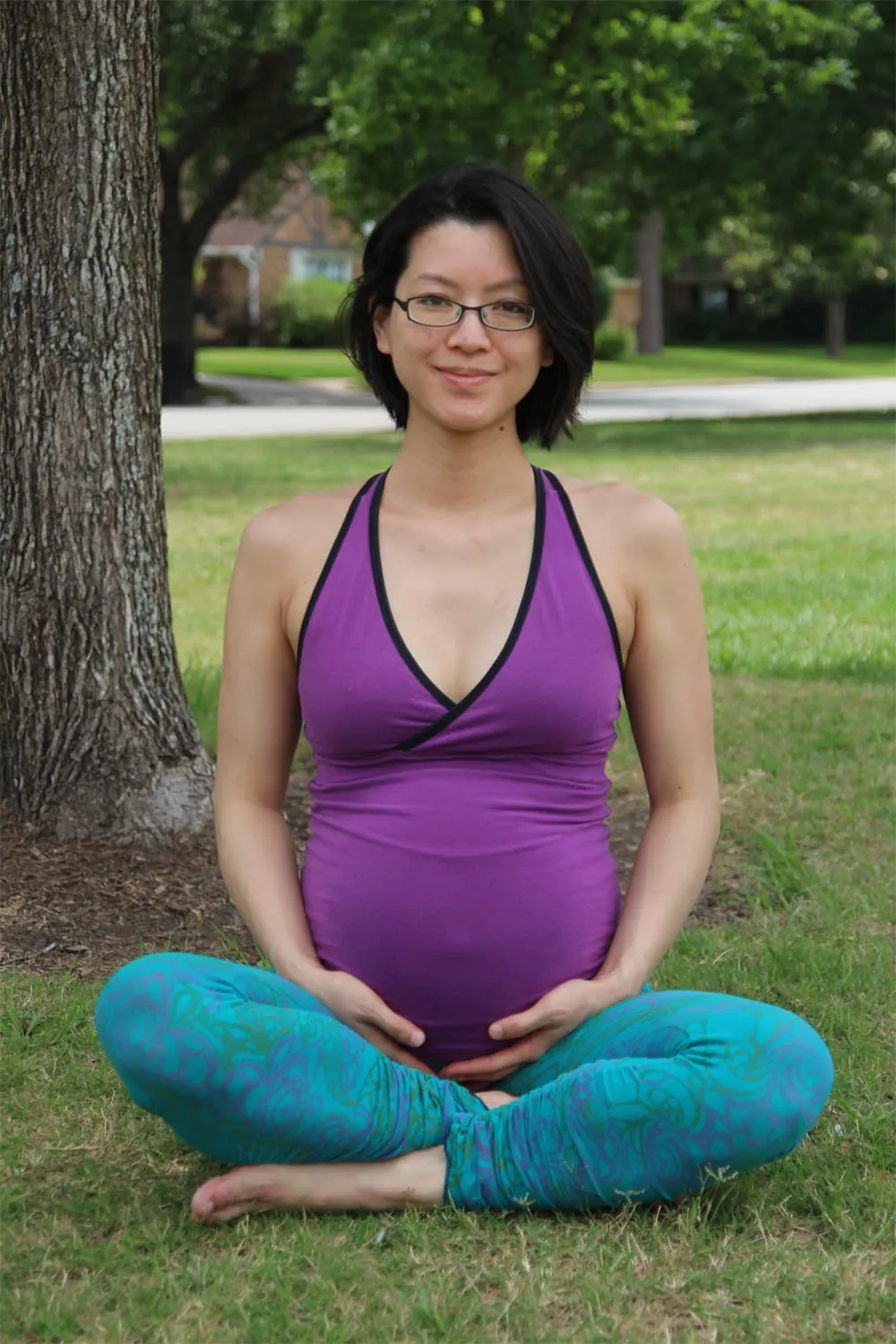 Cat, pregnant, seated cross-legged with her hands resting on her belly
